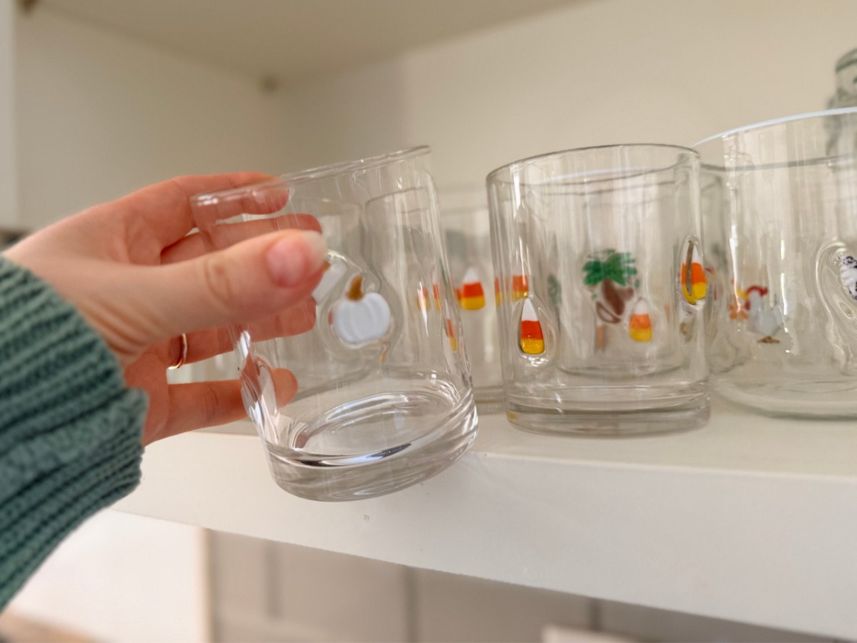 hand grabbing pumpkin icon glass from kitchen cabinet