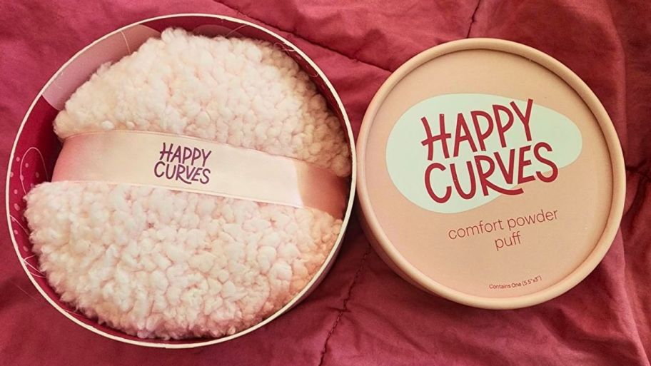 Happy Curves powder and puff on top of the bed