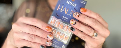 woman with nails decoratged for Halloween holding up a Kiss Haunt Nails package