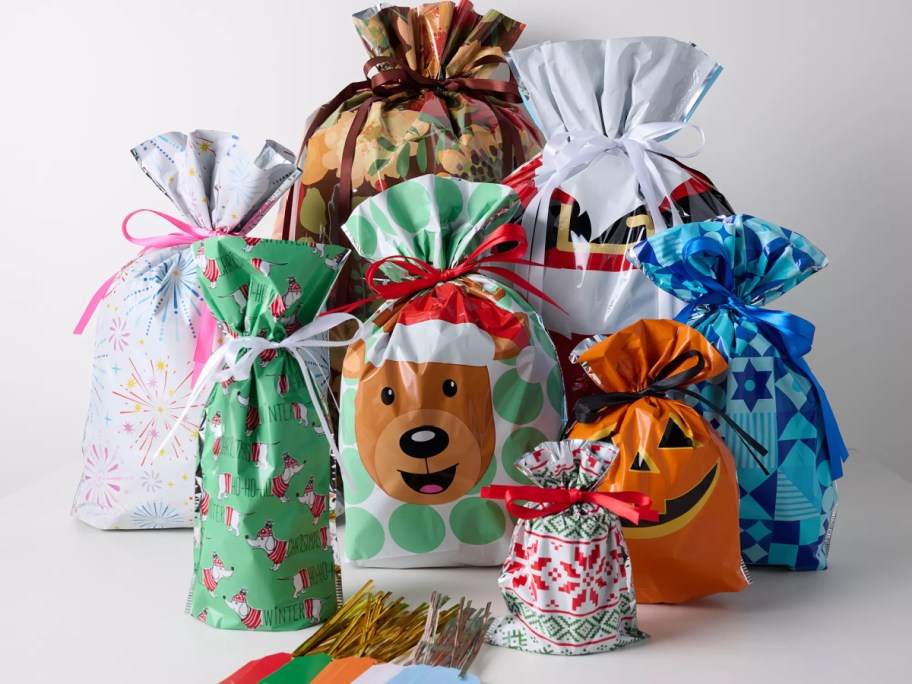 A collection of Kringle Express all-season gift bags and tags in various holiday and celebration designs, tied with ribbons and accompanied by twist ties.
