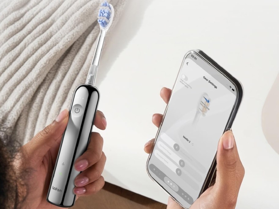 A person holding a stainless steel Laifen Wave Pro electric toothbrush in one hand and a smartphone displaying gear settings app controls in the other.