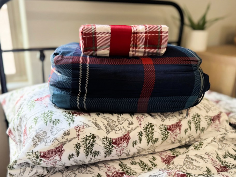 Macy's holiday bedding stacked on bed with Christmas themed sheets