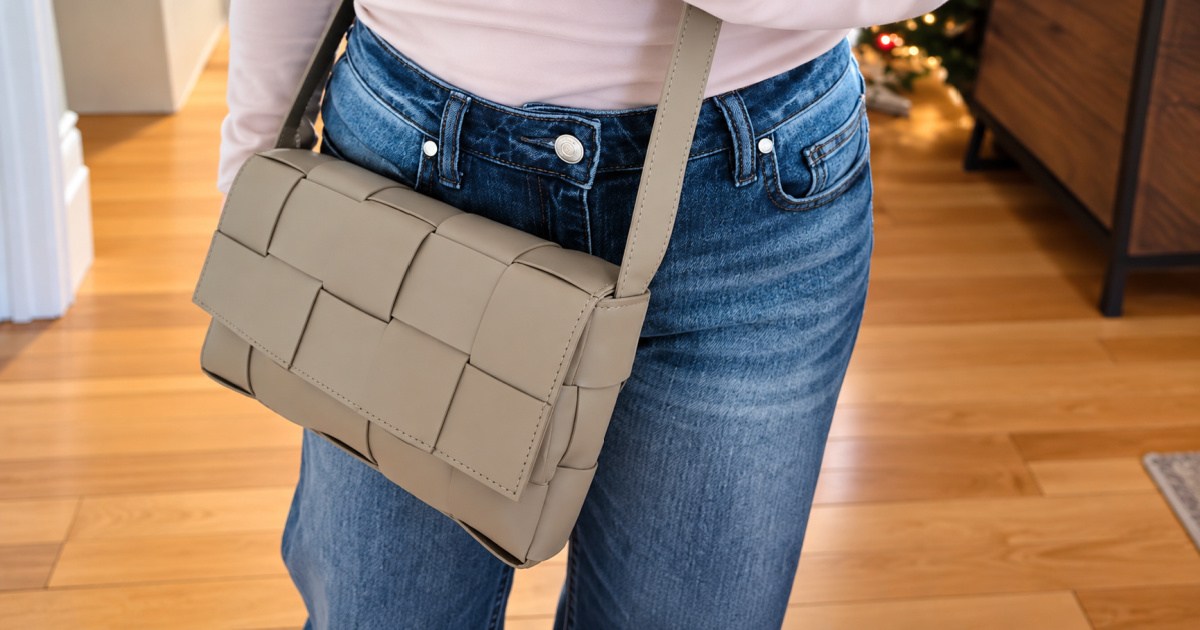 Woman holding tan crossbody purse while wearing blue jeans