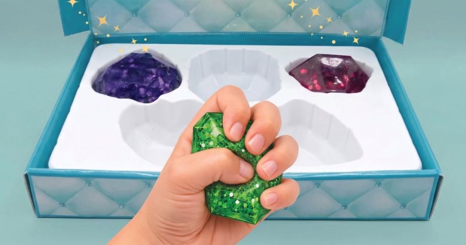 Squeeze Please Gems Collector's Case with 2 Jelly Gems in it and a child's hand squeezing a green jelly gem in front of it