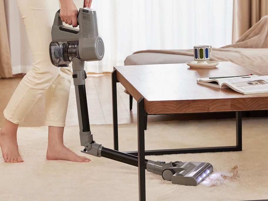woman vacuuming under a coffee table with a cordless vacuum with a bend in the stick