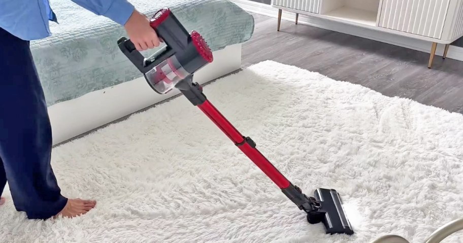woman using a grey and red cordless vacuum on carpet