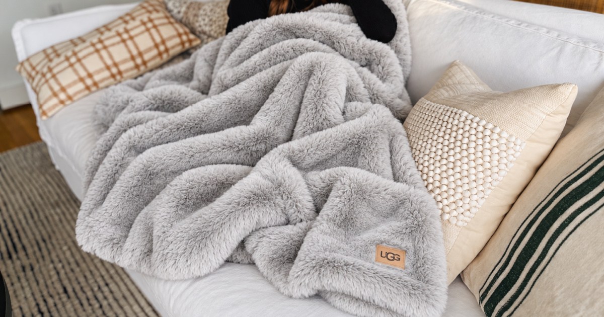Woman on couch snuggling with gray Ugg throw blanket