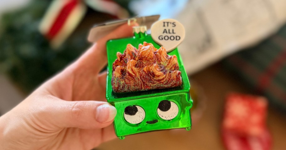 hand holding Wondershop Glass Dumpster Fire Ornament in front of target bag