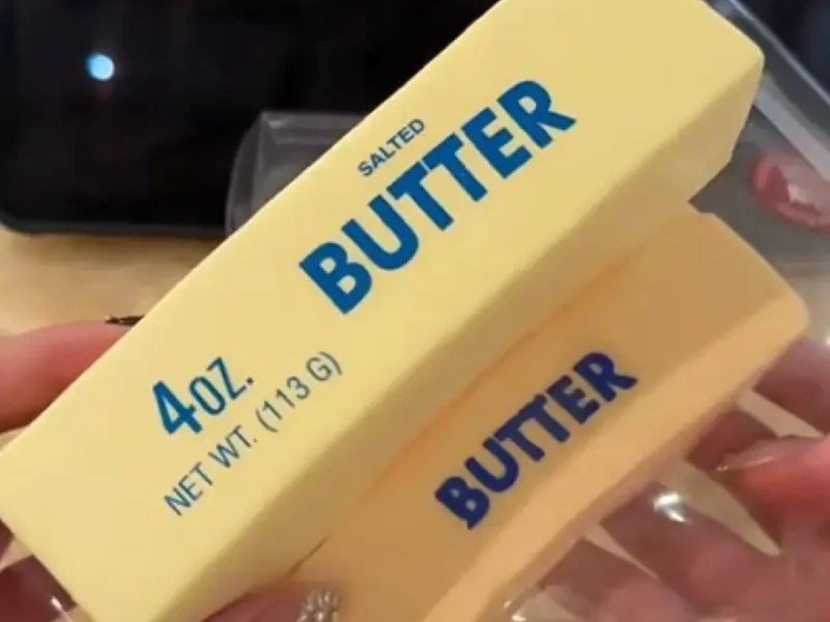 Two yellow butter squishy toys shaped like sticks of salted butter with blue lettering labeled "4oz. Butter" being held by hands.