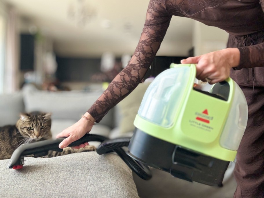 woman using a Bissell Little Green Machine cleaner to clean a pet stain off her sofa