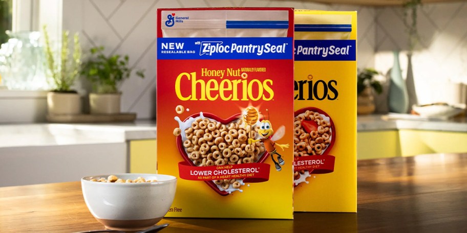 two boxes of cheerios cereal on the table with a bowl of cereal 