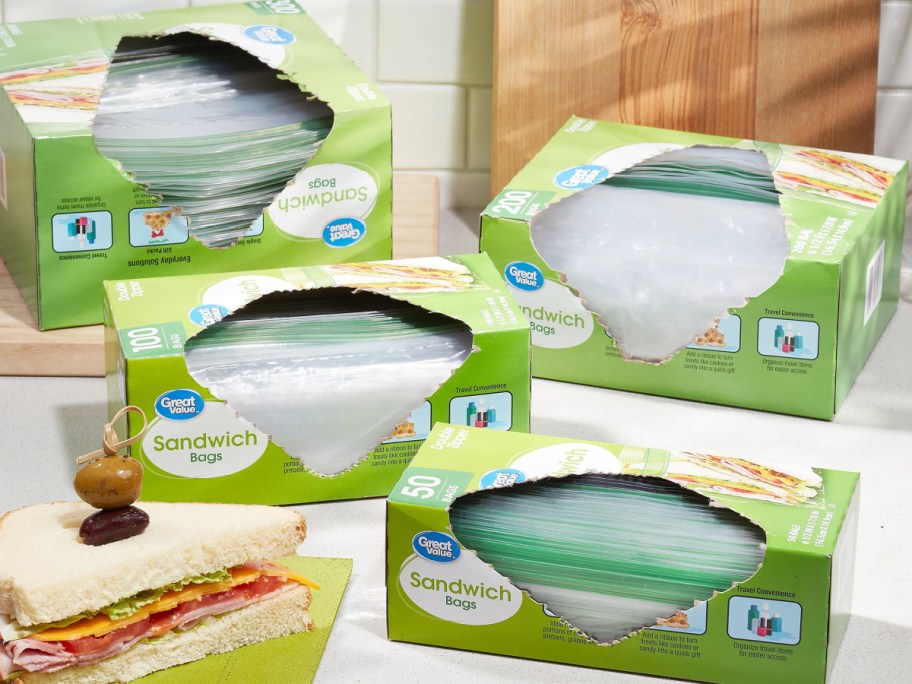 Several green Great Value sandwich bag boxes stacked together on a counter next to a prepared sandwich.
