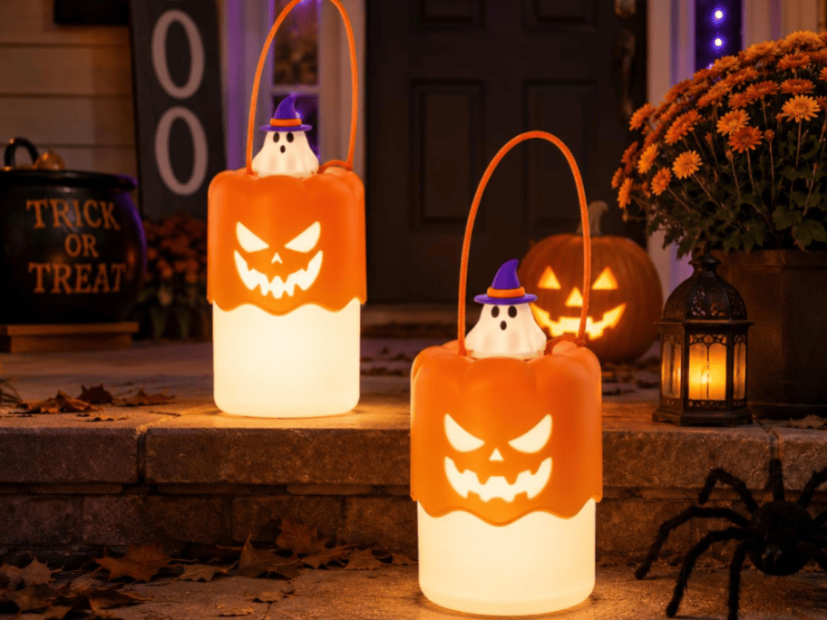 2 pumpkin lanterns lit on a porch decorated for halloween