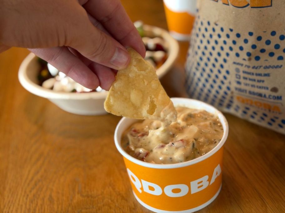 hand holding a tortilla chip and dipping it into queso from qdoba