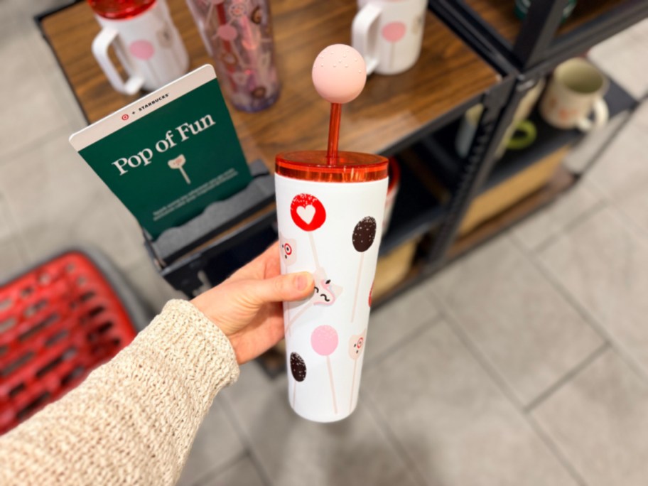 A person holding a Starbucks cake pop-themed tumbler with a straw topper next to a Pop of Fun display sign.