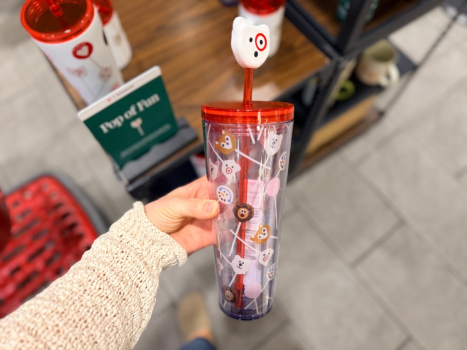 A person holding a clear Starbucks tumbler with animal-themed cake pop designs and a white animal straw topper next to a Pop of Fun display sign.