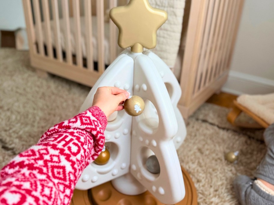 a hand reaching for a toy ornament on a child's toy Christmas tree