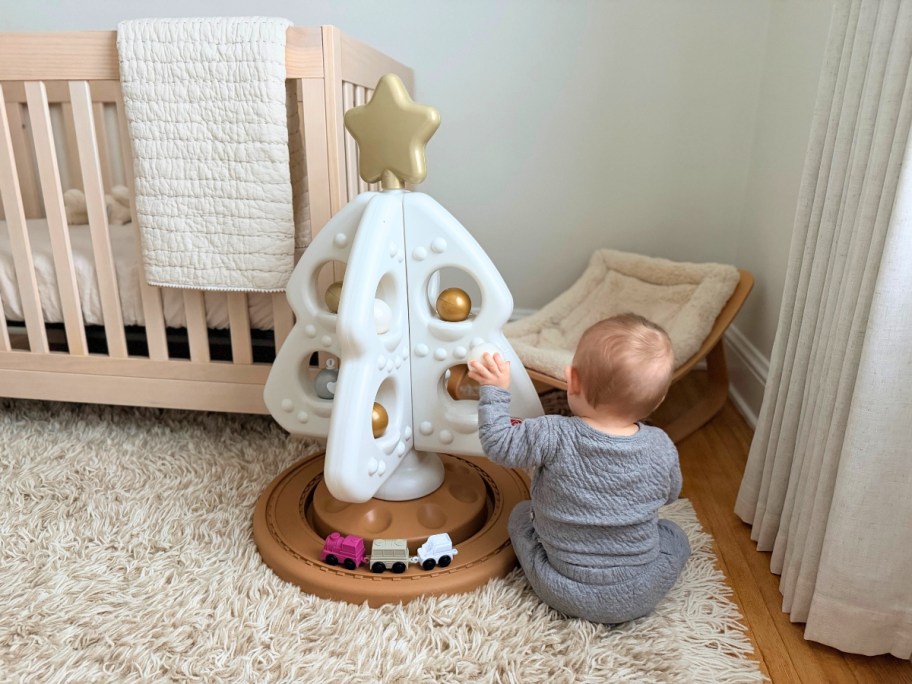 a baby playing with a white, tan, and gold play Christmas Tree