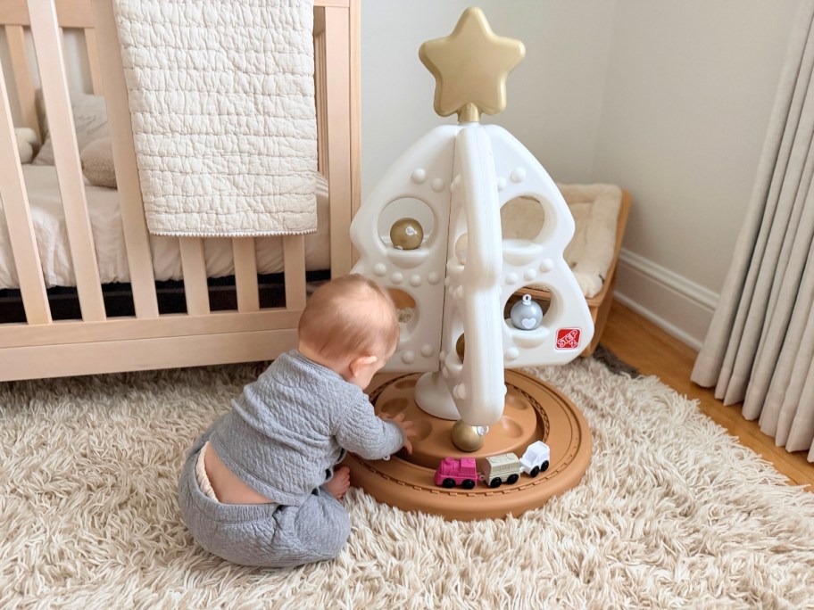a baby playing with a white, tan, and gold play Christmas Tree