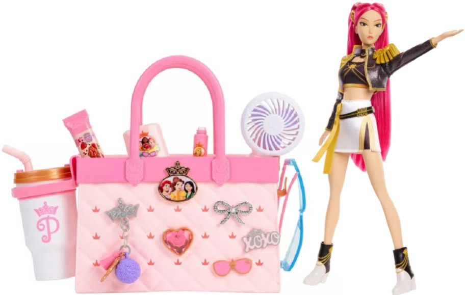 A pink princess-themed purse toy with charms, accessories, and a cup, displayed next to a fashion doll with pink hair and a stylish outfit.