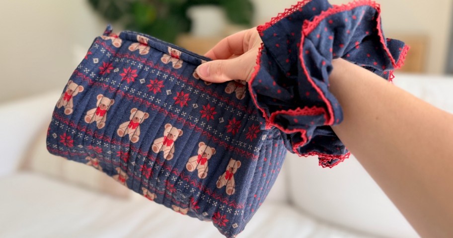 hand with a blue and red hair scrunchie on the wrist and holding a holiday teddy bear zipper pouch