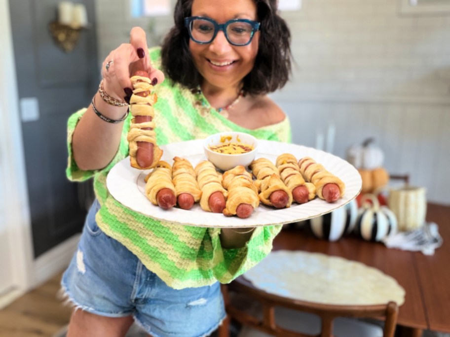 woman holding a platter of halloween mummy hot dogs (