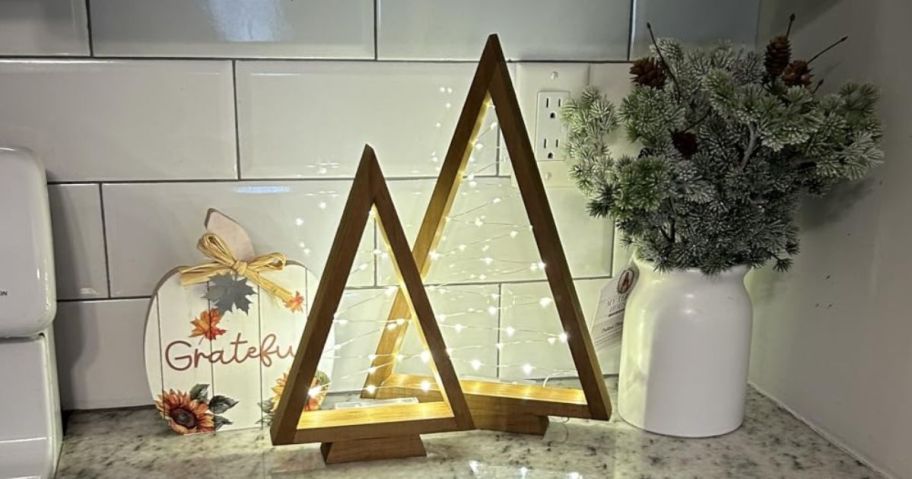 2 wooden light-up christmas trees on a kitchen counter